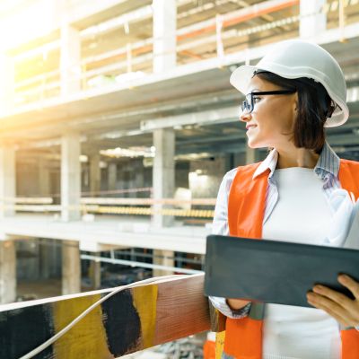 Portrait of adult female builder, engineer, architect, inspector, manager at construction site. Woman with plan, digital tablet