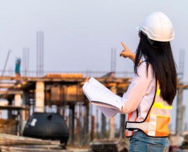 Construction Engineering Asian woman civil engineer paper plan building architect wearing white safety helmet look at the construction site.